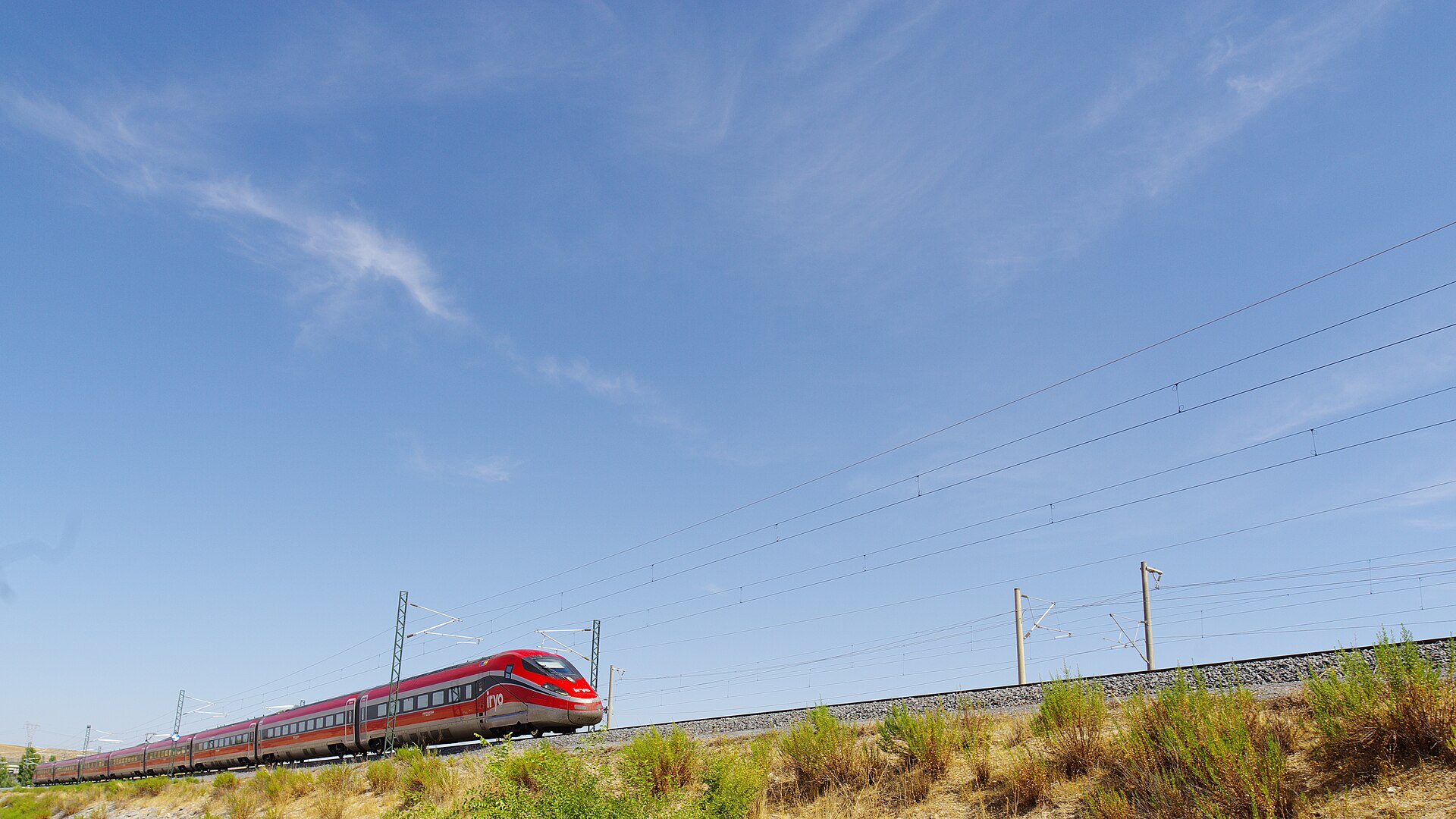 Trains from Madrid: AVE, Iryo, Ouigo and Every Route Explained 3 A red Iryo Frecciarossa 1000 high-speed train running along an embankment under a wide blue sky on the southern edge of Madrid