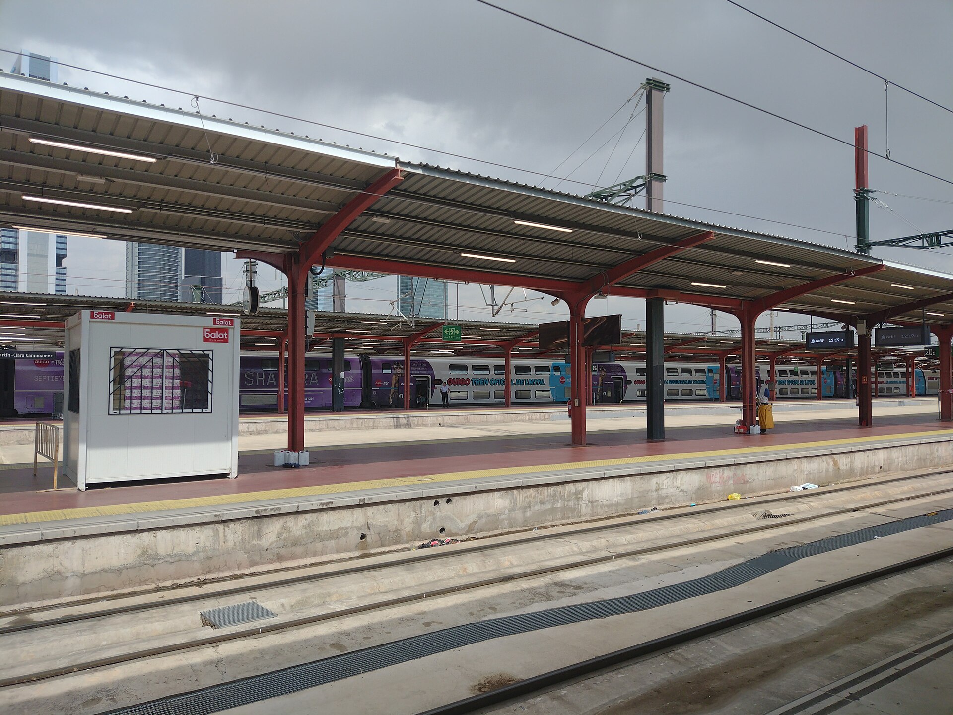 Trains from Madrid: AVE, Iryo, Ouigo and Every Route Explained 4 Covered platforms at Madrid Chamartín-Clara Campoamor station with a purple-liveried Ouigo double-decker train and the Cuatro Torres skyscrapers behind