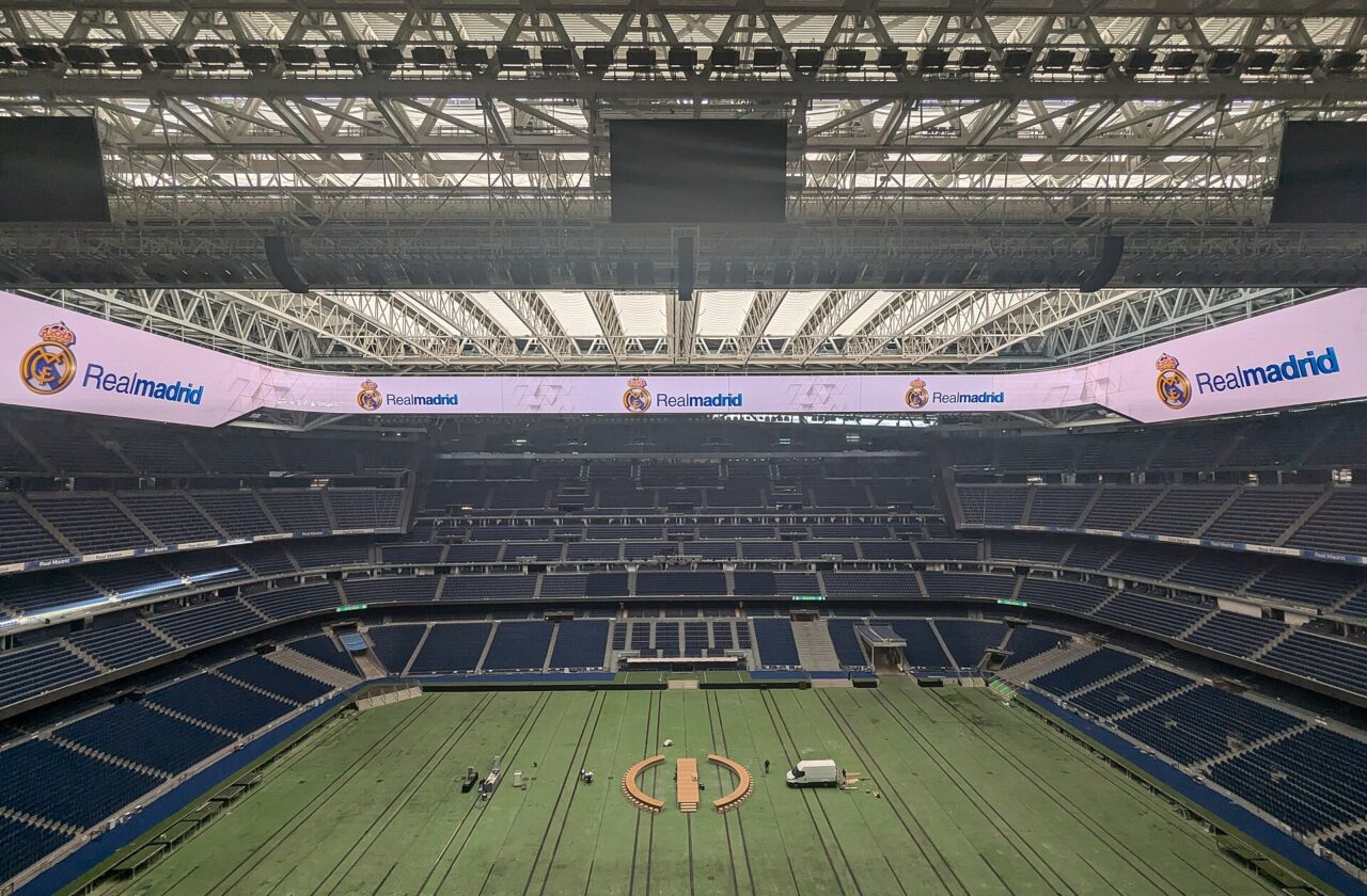 The inside of a large stadium with blue seats, a closed roof and a covered pitch