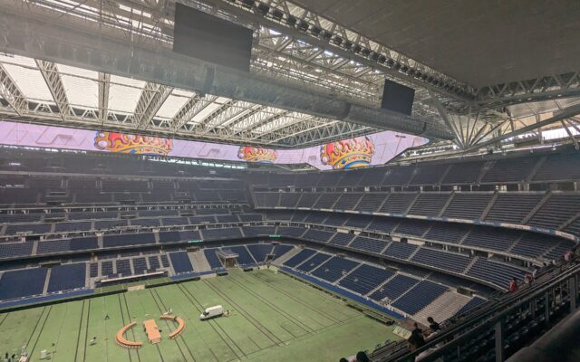 The inside of a large stadium with blue seats, a covered pitch and a video screen running around the roof