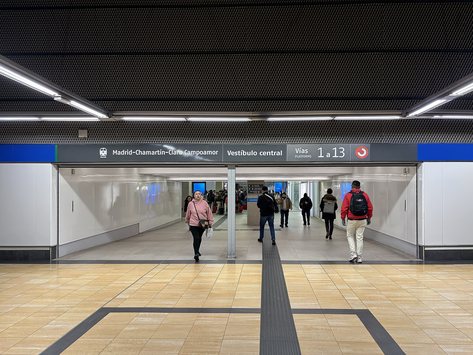 Passengers walking through a passage under a sign reading Madrid-Chamartín-Clara Campoamor, Vestíbulo central, platforms 1 to 13